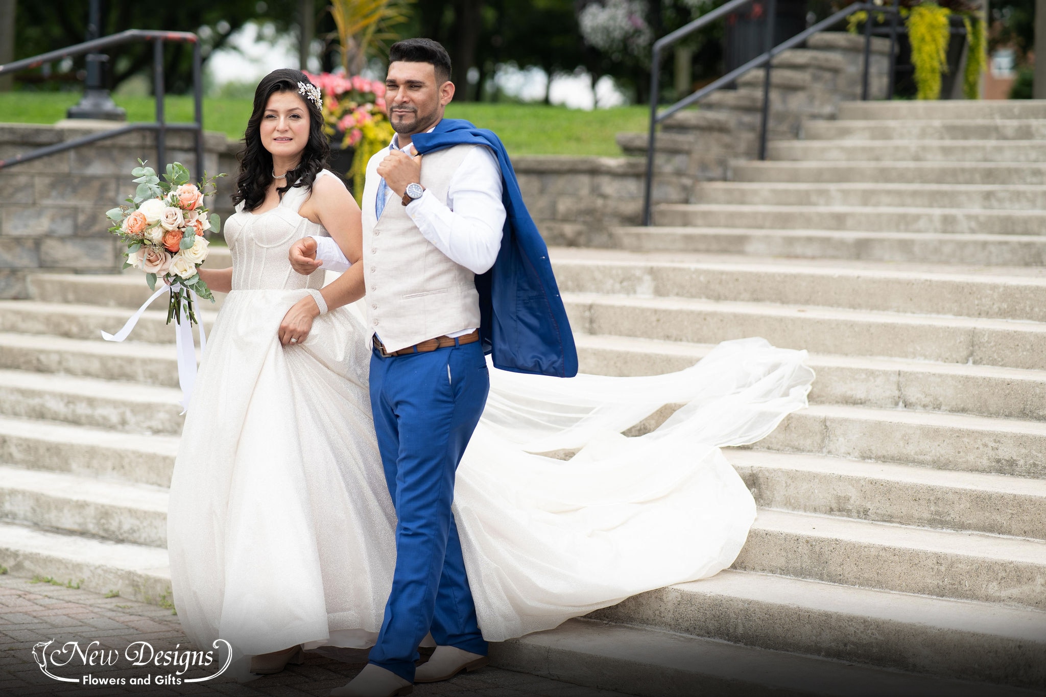 A bride and groom walk down concrete stairs as she holds her bouquet of full white nude and orangey pink roses